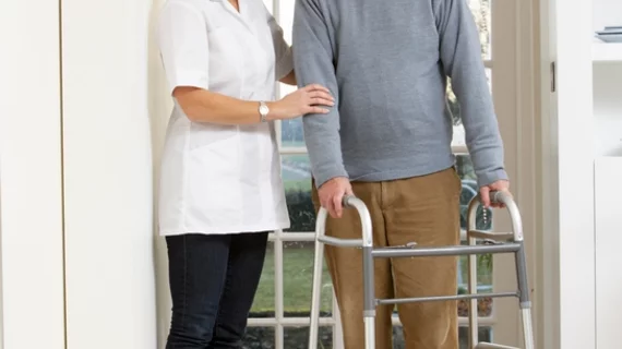 Nurse helps elderly man with walker.